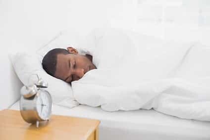 Young man sleeping in bed with alarm clock in foreground at bedroom